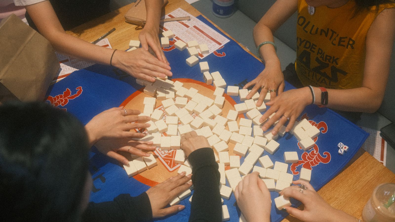 eight hands shuffling mahjong tiles across the table